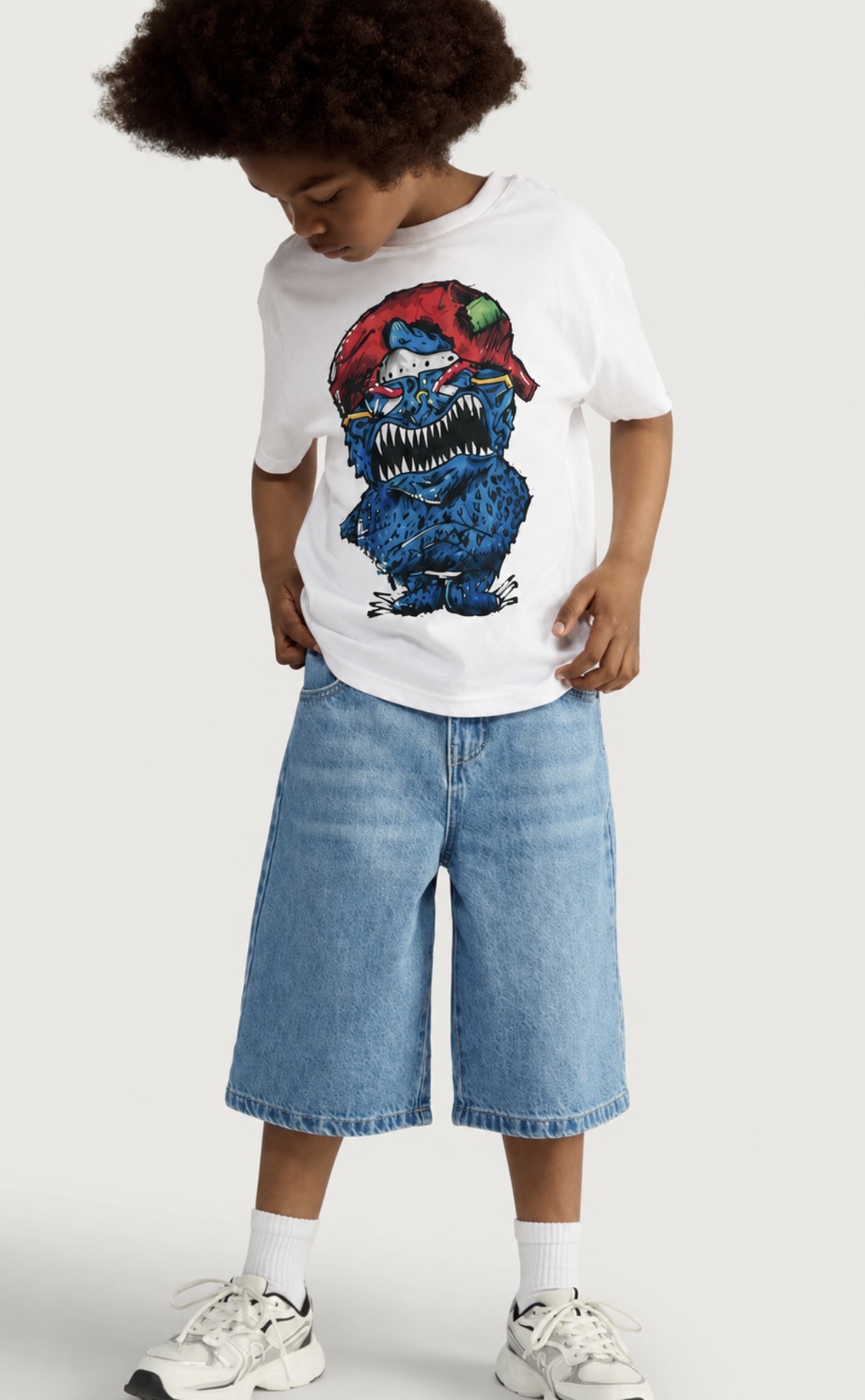A child wearing a white CC Illustrations t-shirt printed with a blue hand-drawn monster in a red baseball cap.